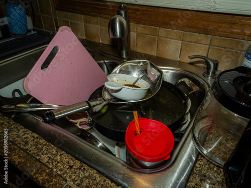 Valokuva Messy stainless steel kitchen sink piled high with dirty dishes including frying