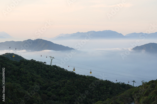 Slika na platnu Spectacular view of cable car cabins gliding over a lush green forest with foggy