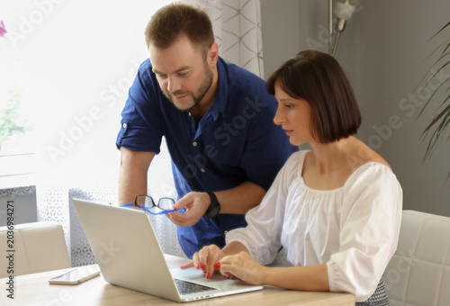 Foto A woman at a table uses a laptop and consults with a man.