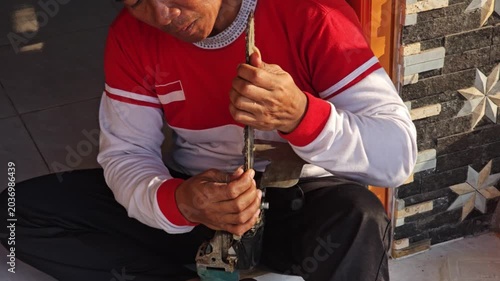 Man in red and white long sleeve shirt using screwdriver to disassemble angle grinder while sitting on floor
