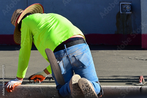 Schilderij op canvas Construction worker kneeling beside a curb at a commercial development site adja
