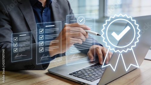 Business professional using digital stylus to sign electronic documents on laptop with holographic checkmarks and certification seal representing secure online contracts and legal
