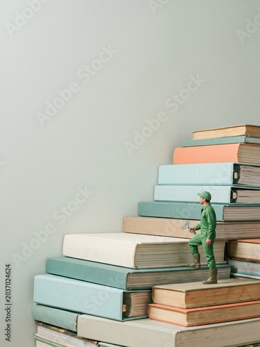 Large pale grey wall background with copy space behind a small person climbing a staircase made of books for landscape industry marketing and irrigation business concepts