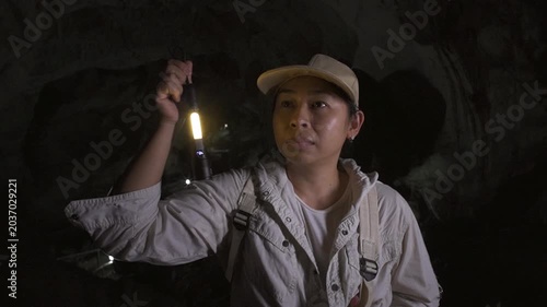 Asian woman adventurer exploring a dark underground cave with a flashlight.
