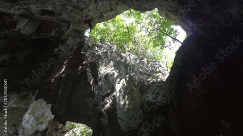 Low angle view of a large cave skylight with natural light streaming into the dark cavern.