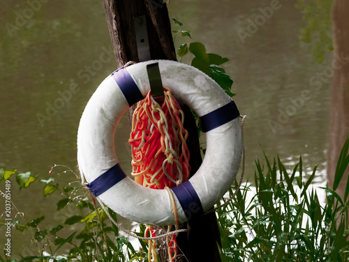 Φωτογραφία White and blue lifebuoy ring with orange rescue rope hanging on a wooden post by