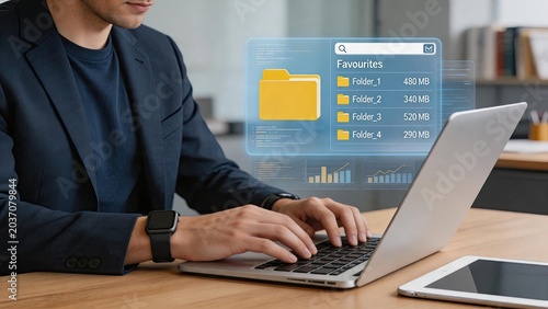 Professional man working on laptop with futuristic holographic file folder interface, cloud storage data management concept, virtual reality screen displaying folders and charts