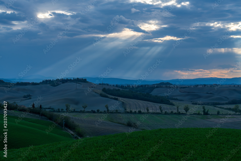 Obraz premium Dramatic sunbeams breaking through clouds over Tuscany rolling hills landscape, Italy