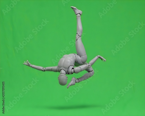 A widescreen, horizontal layout capturing a grey articulated mannequin suspended upside down in mid-air, creating a highly cinematic action sequence. The figure's back is severely arched with its head