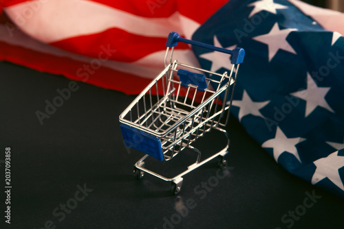 Shopping cart and American flag on black background, closeup view