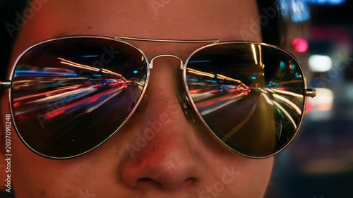 Fluffy rich cats in sunglasses and chains riding luxury open car concept. Close up of reflective aviator sunglasses showing vibrant city lights and motion blur at night