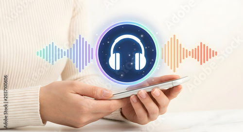 Person holding smartphone with holographic headphone audio waveform for music streaming podcast listening voice assistant and digital sound recognition technology and mobile app experience