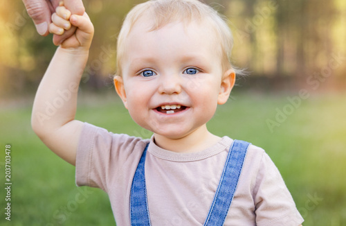 A toddler walks hand in hand with his father, smiling at the camera.