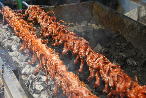 Billede på lærred Close up of traditional Thai style marinated chicken pieces or giblets on long bamboo skewers, roasting over an open charcoal grill with smoke at a local night market