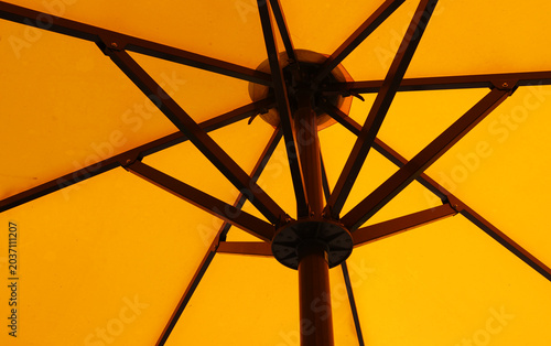 A low-angle view looking up at the metal rib structure under a bright yellow patio umbrella