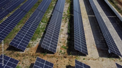 Aerial tracking shot of solar panel rows moving over rural solar farm field during sunny daytime