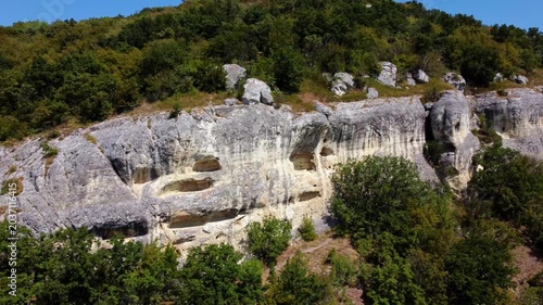 Aerial tracking shot of limestone cliff face panning across wooded hillside under clear blue sky