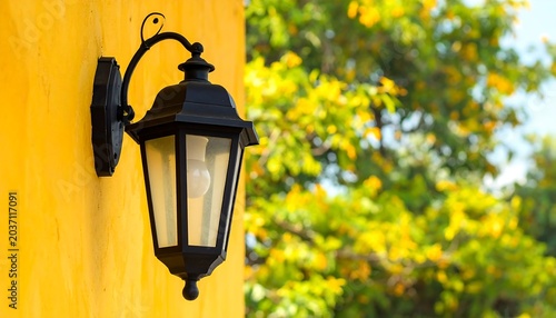Close-up of a black lantern affixed to a vibrant yellow exterior wall, with blurred green foliage in the background