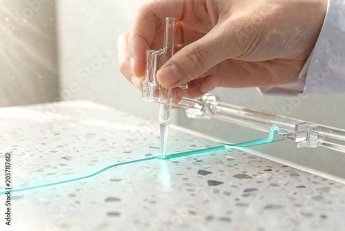 Hand precisely manipulating blue liquid with scientific tool