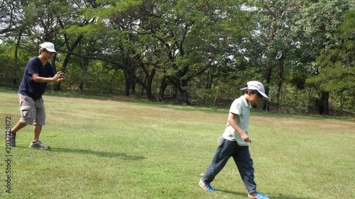 Happy little boy playing with a boomerang in the park while his father takes a photo with a smartphone. 4k
