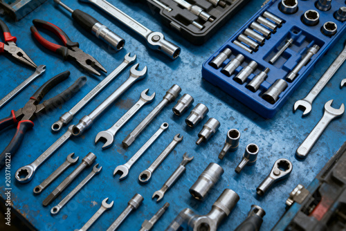 Set of metal hand tools including wrenches, pliers, and sockets arranged on a blue surface
