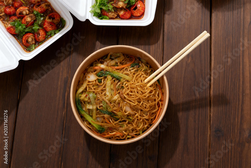 Takeout Asian noodle dish with vegetables and shrimp in plastic containers on wooden table