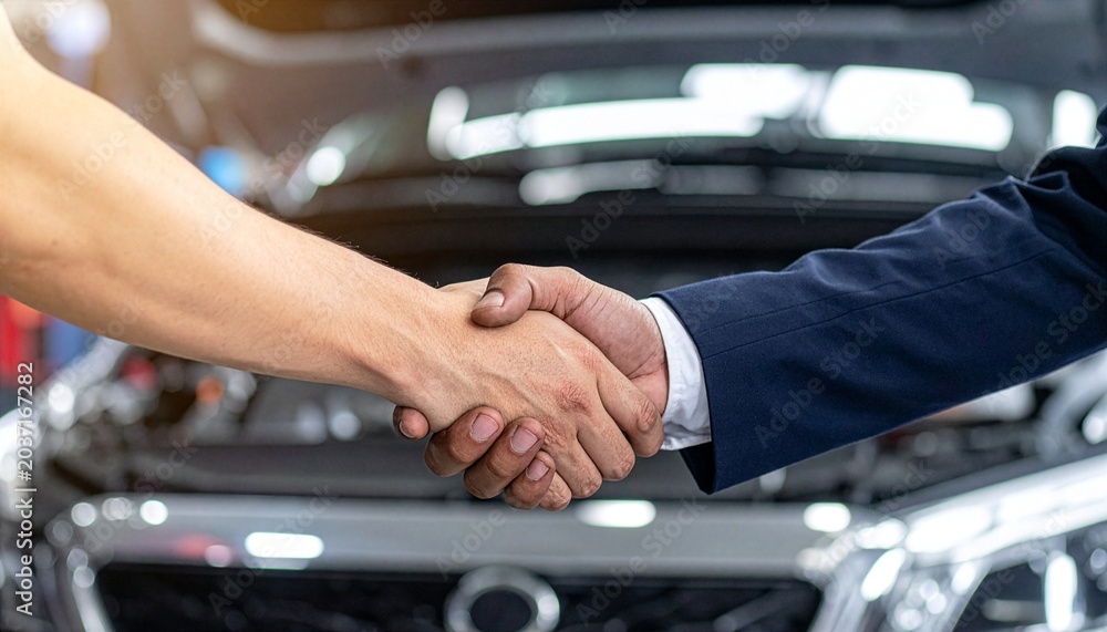 Naklejka premium Close-up of a confident business handshake between a car dealer and a customer with a blurred luxury vehicle background, symbolizing trust, successful auto sale, and financial agreement.