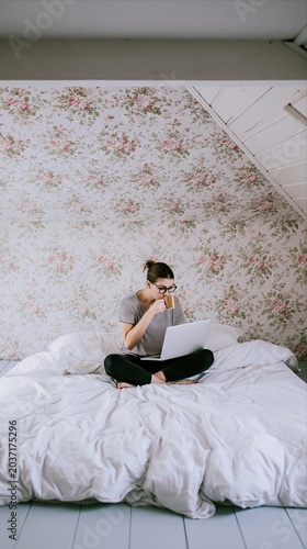 Young woman working remotely from bed while drinking coffee at home
