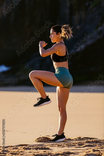 Athletic woman performing high knee exercise on beach at sunset