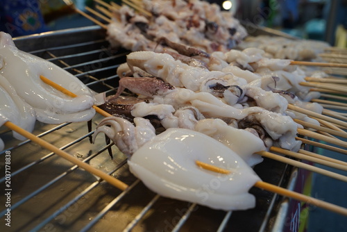 Close up full frame of fresh, clean white raw squids and cuttlefish on sticks ready for customers to order at a night market seafood stall.