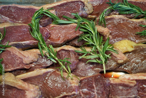 Close up full frame of uncooked raw beef steak meat seasoned and topped with fresh green rosemary herbs, ready for grilling or cooking.