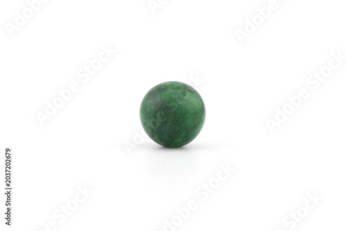 A green sphere made of imperial jade rests on a smooth white surface. The object is round and has a deep green color. Sunlight reflects on its surface