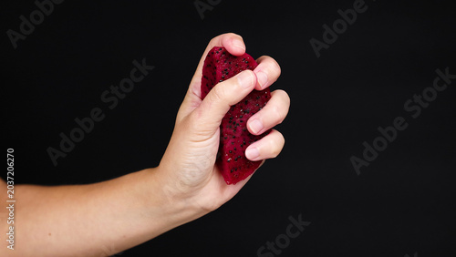 Foto Hand Squeezing a Slice of Red Dragon Fruit Against Black Background