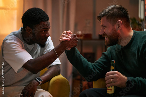 Foto Young adult Black man and Caucasian man clasping hands while socializing at home, expressing male friendship and bonding