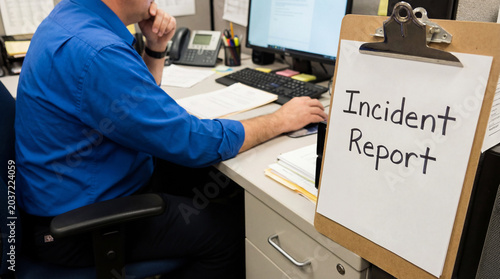 Worker sitting at desk, drafting incident report, using computer for documentation in an office environment