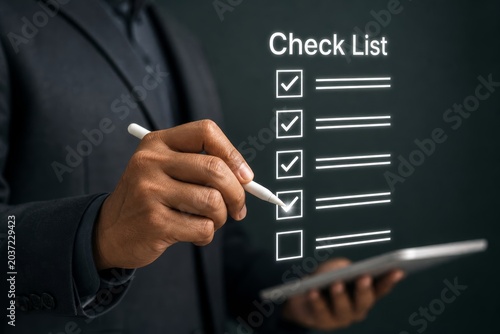 Man in a suit uses a stylus to mark a completed task on a glowing checklist displayed digitally on a dark background with a tablet in hand.
