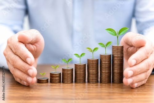 Man's hands gently cupping a row of stacked coins with small plants growing from them, symbolizing financial growth and investment.