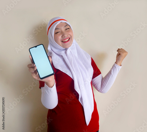Young Asian Girl Wearing White and Red Clothes With Headband Showing Blank Screen Phone For Mockup Or Ads.