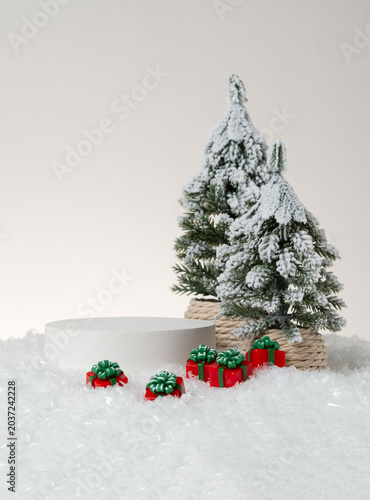 Canvastavla Christmas product display photography featuring a white cylindrical podium with red wrapped gift boxes with green bows and a snow-covered pine tree in a rope pot on a clean neutral studio background