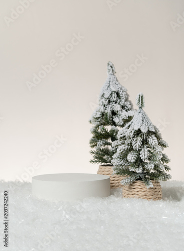 Konstfotografi Vertical Christmas product display scene featuring a white cylindrical podium beside a snow-covered pine tree in a rope-wrapped pot, shot on a clean neutral studio background with copy space