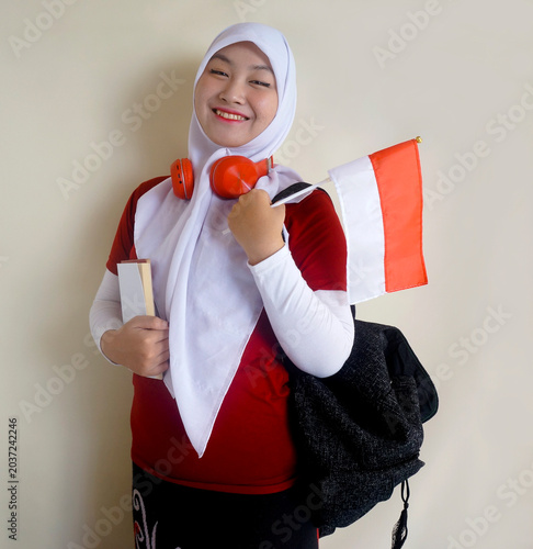 Young Asian College Girl Holding Little Flag And Books Looking At Camera With Happy Expression. Indonesia Independence Day Celebration