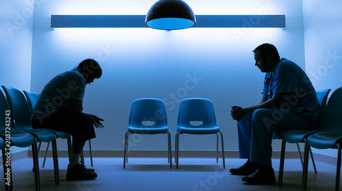 Compassionate psychiatric nurse sitting beside distressed patient in hospital intake area under fluorescent lights offering calm support