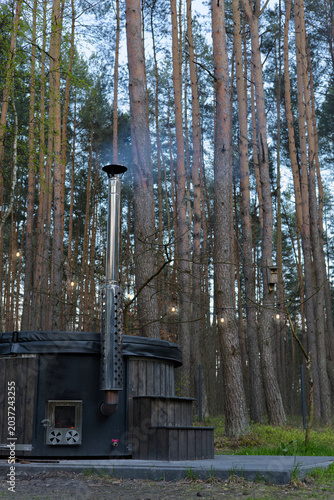 Vertical view of the luxurious, outdoor wood-burned jacuzzi with tall coniferous trees in the background