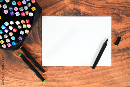 blank sheet of paper lies in the center of the table surrounded by professional sketching markers