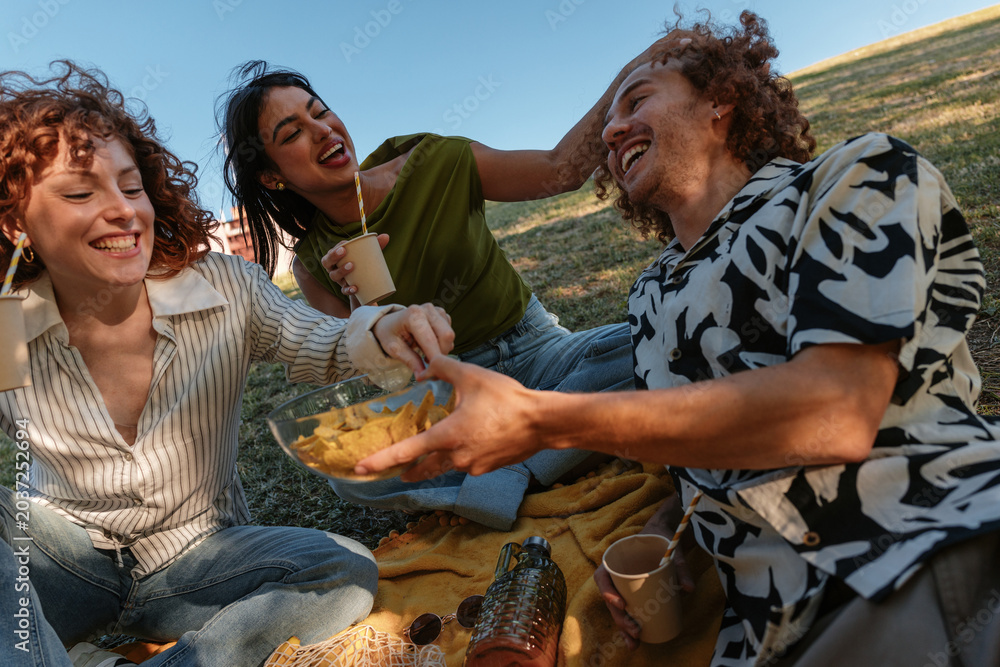 Obraz premium Young friends laughing and sharing snacks during picnic