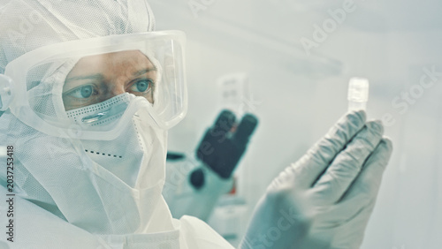 A scientist in a clean suit examines a sample, surrounded by sterile laboratory equipment, highlighting the precision needed in biotechnology and microbiology research.