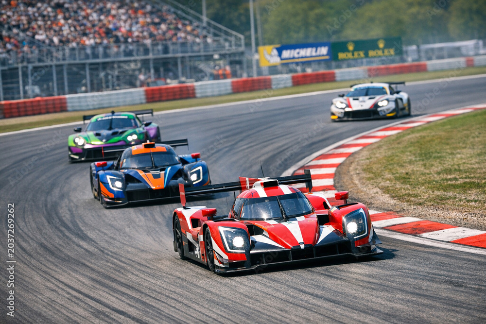 Obraz premium A dynamic scene from a Formula One race track. Cars are in motion, navigating sharp turns on the asphalt with fans and advertising boards in the background.