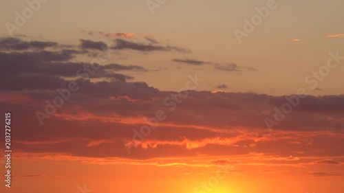 Orange sunset sky with moving clouds.