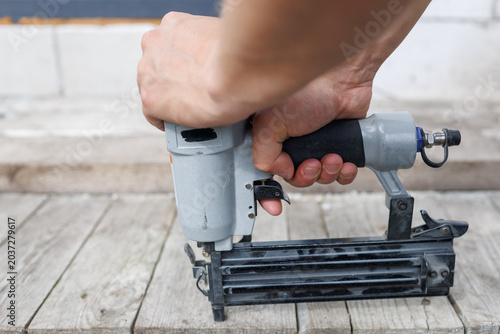 A close-up view of a pneumatic nail gun being pressed down onto horizontal wooden flooring boards