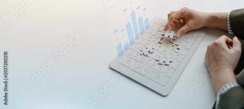Business professional arranging puzzle pieces on keyboard with digital graph overlay, representing data analysis, financial growth, strategic planning, and technology solutions.